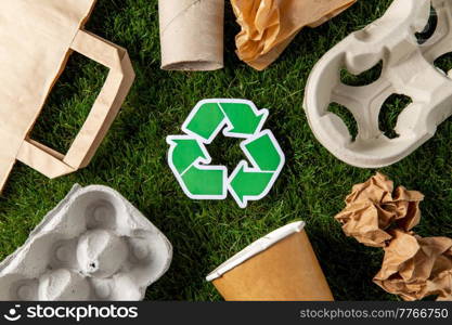 environment, sustainability and ecology concept - close up of green recycling sign and paper waste on grass. green recycling sign and paper waste on grass