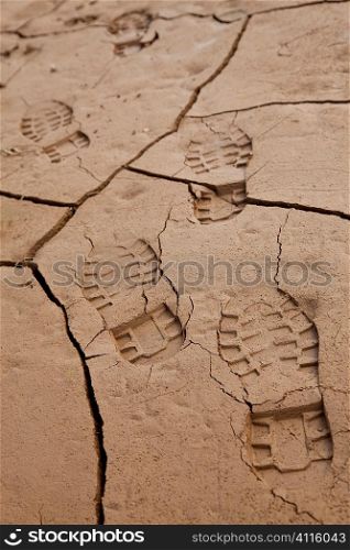 Environmental concept shot showing bootprints going across cracked dry earth in dried up lake bed or riverbed.