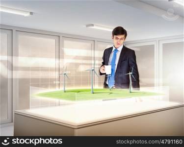 Environmental problems and high-tech innovations. Image of young businessman looking at high-tech picture of windmills