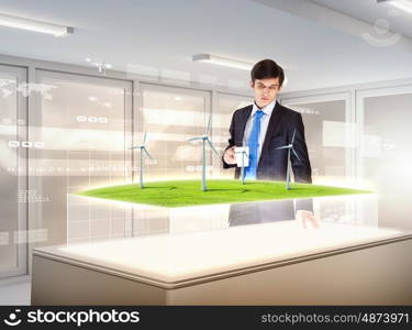 Environmental problems and high-tech innovations. Image of young businessman looking at high-tech picture of windmills