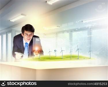 Environmental problems and high-tech innovations. Image of young businessman looking at high-tech picture of windmills