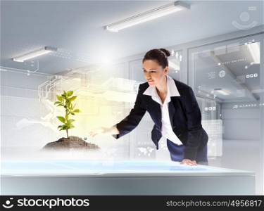 Environmental problems and high-tech innovations. Image of young businesswoman touching sprout on high-tech picture