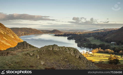 Epic Autumn Fall landscape of Ullswater and surrounding mountains and hills viewed from Hallin Fell on a crisp cold morning with stunning sunlgiht hitting the slopes