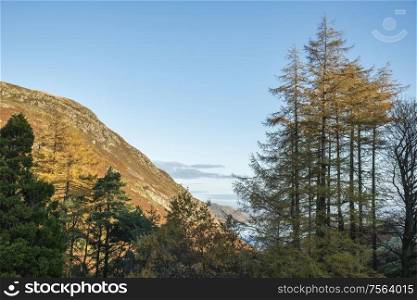 Epic Autumn Fall landscape of Ullswater and surrounding mountains and hills viewed from Hallin Fell on a crisp cold morning with stunning sunlgiht hitting the slopes