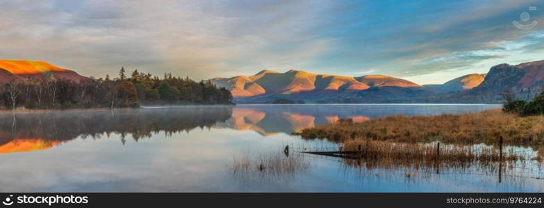 Epic Autumn sunrise landscape image looking from Manesty Park in Lake Distict towards sunlit Skiddaw Range with mit rolling across Derwentwater surface