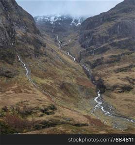 Epic dramatic landscape image of Three Sisters in Glencoe in Scottish Highlands on a wet Winter day