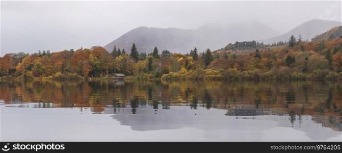 Epic landscape image of Catbells viewed acros Derwentwater during Autumn in Lake District with mist rolling across the hills and woodland