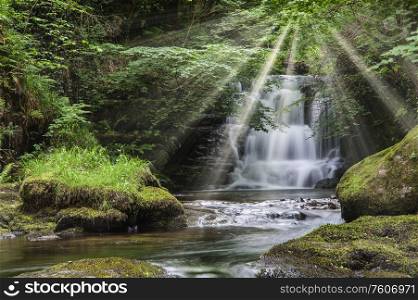 Epic waterfall in forest landscape image with added drama of sun beams breaking through trees in woodland