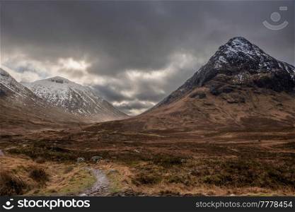 Epic Winter landscape image of Etive Mor in Scottish Highlands with sunbeams streaming down between the mountain peaks