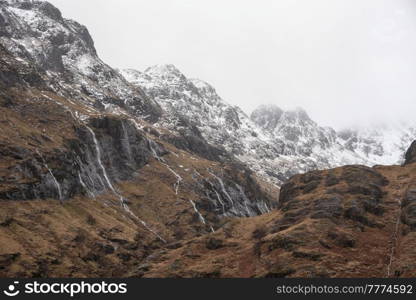 Epic Winter landscape image of snowcapped Three Sisters mountain range in Glencoe Scottish Highands with dramatic sky