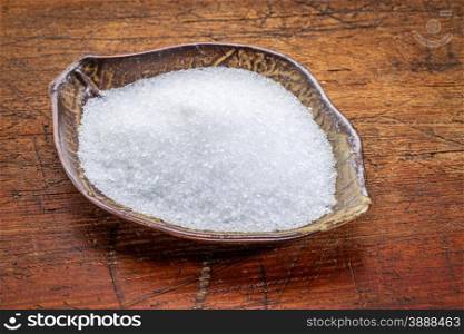 Epsom salts (Magnesium sulfate) in a leaf shaped ceramic bowl against rustic wood - relaxing bath concept