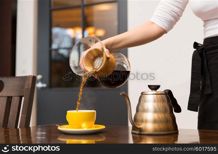 equipment, coffee shop, people and technology concept - close up of barista woman with glass coffeemaker and pot pouring hot coffee to cup at cafe bar or restaurant kitchen