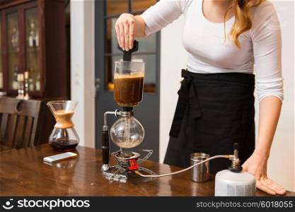 equipment, coffee shop, people and technology concept - close up of barista woman stirring coffee grounds in siphon coffeemaker top vessel at cafe bar or restaurant kitchen