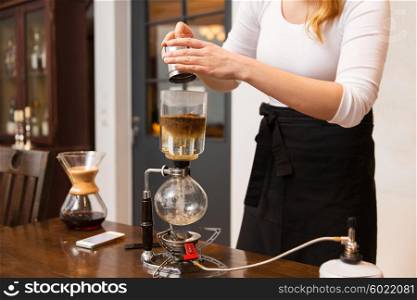 equipment, coffee shop, people and technology concept - close up of barista woman with pot pouring ground coffee to siphon coffeemaker at cafe bar or restaurant kitchen