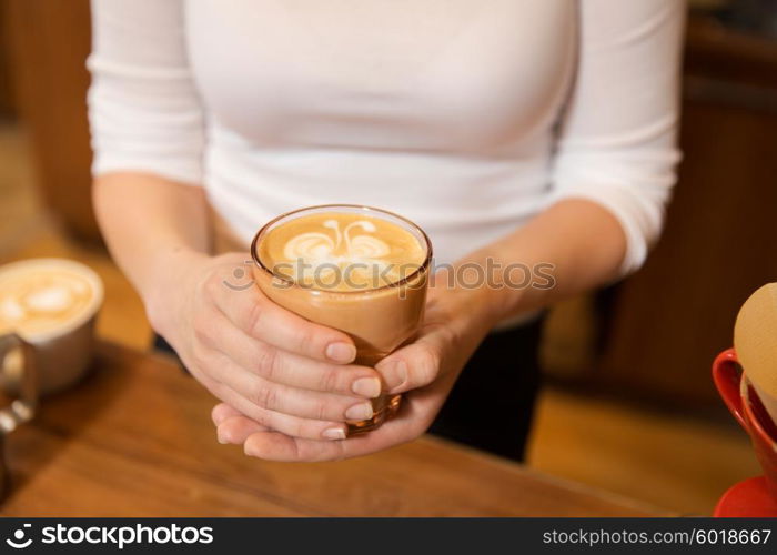 equipment, coffee shop, people and technology concept - close up of hands with latte art etching in coffee cup