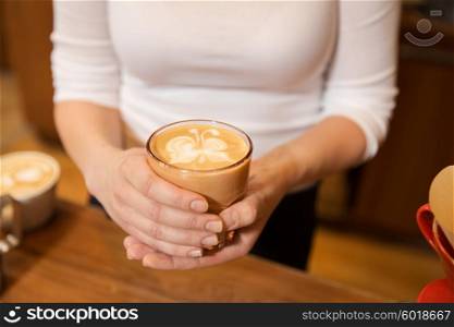 equipment, coffee shop, people and technology concept - close up of hands with latte art etching in coffee cup