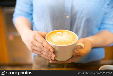 equipment, coffee shop, people and technology concept - close up of hands with latte art etching in coffee cup