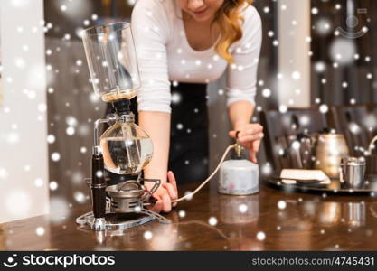 equipment, coffee shop, people and technology concept - close up of woman with butane gas burner heating water in siphon coffeemaker at cafe bar or restaurant kitchen over snow