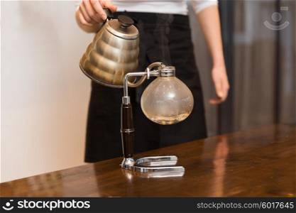 equipment, coffee shop, people and technology concept - close up of woman with pot pouring hot water to chemex coffeemaker filter at cafe bar or restaurant kitchen