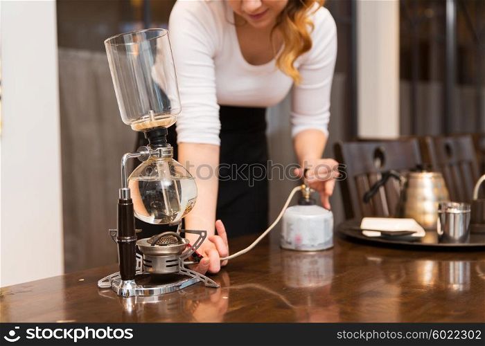 equipment, coffee shop, people and technology concept - close up of woman with butane gas burner heating water in siphon coffeemaker at cafe bar or restaurant kitchen