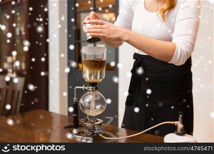 equipment, people and technology concept - close up of woman with pot pouring ground coffee to siphon coffeemaker at cafe bar or restaurant kitchen over snow