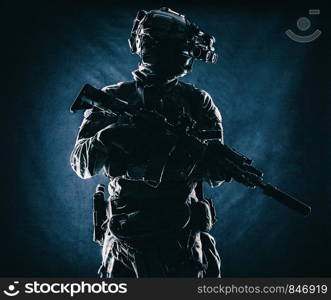 Equipped modern ammunition, armed assault rifle with silencer, standing in darkness with four lenses night vision goggles on battle helmet commando soldier low key, studio portrait on black background. Commando with night vision goggles studio shoot