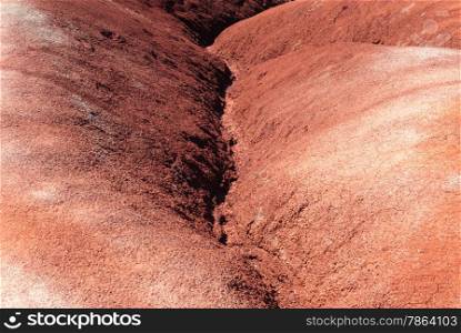 Eroded water channel between red clay badlands dunes.