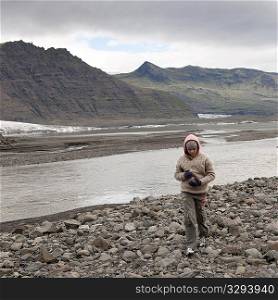 Eroding mountain next to glacial riverbank and rocky moraine with girl