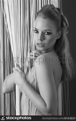 erotic blonde girl in glamour indoor portrait with freckles on face and fashion make-up. In sexy pose she is covering her naked breast and looking in camera ,black and white image&#xA;