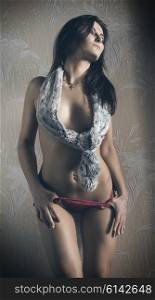 erotic brunette woman taking off her red panties and covering her naked breast with fur scarf. In sexy pose