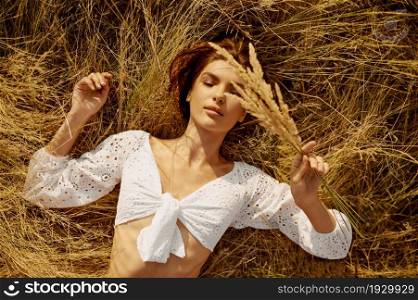 Erotic woman in lingerie lying in the hay in the field, top view. Sexy female person with slim body in underwear leisures on meadow, relaxation outdoors, feeling of freedom. Erotic woman in lingerie lying in hay in the field