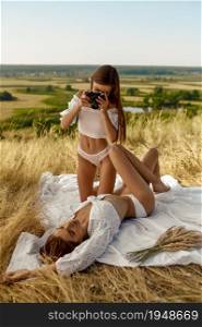 Erotic women in lingerie, photosession in the field. Female persons with slim body in underwear leisures on meadow, relaxation on sunset, feeling of freedom. Erotic women in lingerie, photosession in field