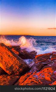 ertical shot of waves splashing to the rock formations during a breathtaking sunset