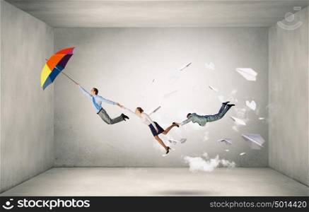 Escape from office. Businesspeople holding each other and flying on colorful umbrella