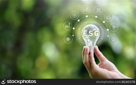 ESG icon concept in hand holding bulb for environmental, social and governance in sustainable and ethical business on networked connections on green background.