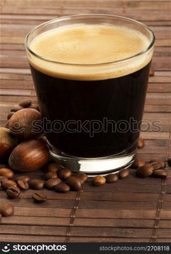 espresso coffee in a short glass with hazelnuts. espresso coffee in a short glass with hazelnuts and coffee beans on wooden background