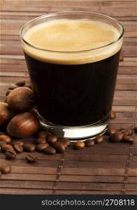 espresso coffee in a short glass with hazelnuts. espresso coffee in a short glass with hazelnuts and coffee beans on wooden background