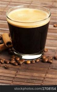 espresso in a short glass with coffee beans and cinnamon from diagonal top. espresso in a short glass with coffee beans and cinnamon sticks from diagonal top on wooden background