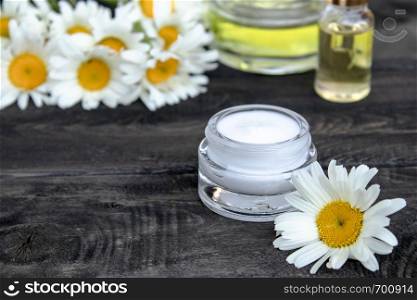 Essential oil and cosmetic cream are on the wooden table near the chamomile flowers.. Essential oil and cosmetic cream are on a wooden table near the flowers of white chamomile.