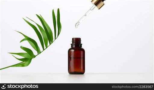 essential oil falling from the amber glass dropper. Blue bottle of cosmetic oil with a pipette, white background