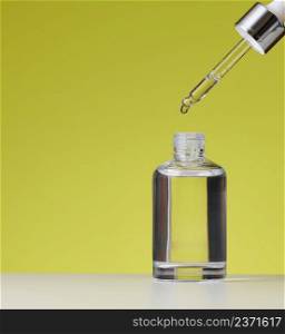 essential oil falling from the amber glass dropper. White bottle of cosmetic oil with a pipette, green background