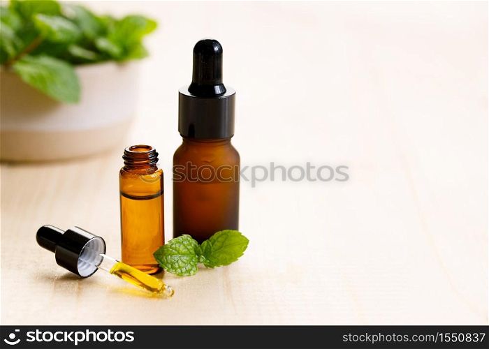 Essential oil in amber glass bottle with fresh green mint leaves on wooden background, with copy space.