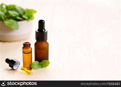 Essential oil in amber glass bottle with fresh green mint leaves on wooden background, with copy space.