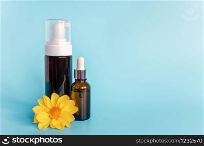 Essential oil in small open brown dropper bottle with lying glass pipette, big bottle with white dispenser and yellow flower on blue background. Concept natural organic beauty cosmetics product.. Essential oil in small open brown dropper bottle with lying glass pipette, big bottle with white dispenser and yellow flower on blue background. Concept natural organic beauty cosmetics product