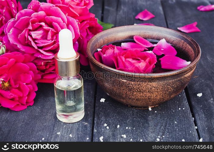 Essential oil near the bowl with red rose petals on a dark wooden background. Aromatherapy.. Essential oil near the bowl with red rose petals on a dark wooden background.