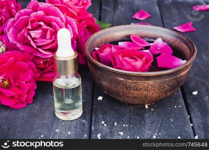Essential oil near the bowl with red rose petals on a dark wooden background. Aromatherapy.. Essential oil near the bowl with red rose petals on a dark wooden background.