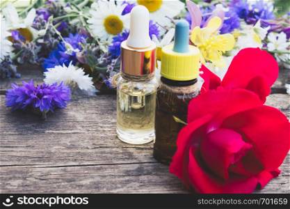 essential oil with a rose in a glass bottle near wildflowers on wooden background. Close-up.. essential oil with a rose in a glass bottle near wildflowers on wooden background.