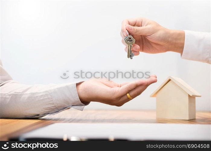 Estate agent in suit sitting in an office desk Handing over of house keys with customer after contract signature.