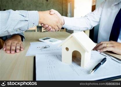 Estate agent in suit sitting in an office desk shaking hands with customer after contract signature.