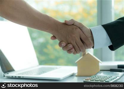 Estate agent sitting in a desk shaking hands with customers after signing a home purchase contract.